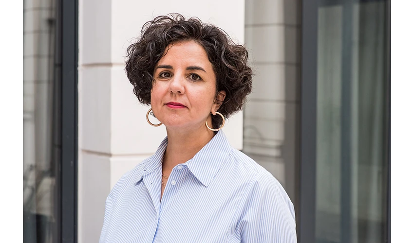 photo of a light skinned woman with short hair wearing a blue and white collared shirt looking at the viewer